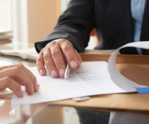 Business people signing a contract Close-up of businessman examining business contract and signing it at the office desk